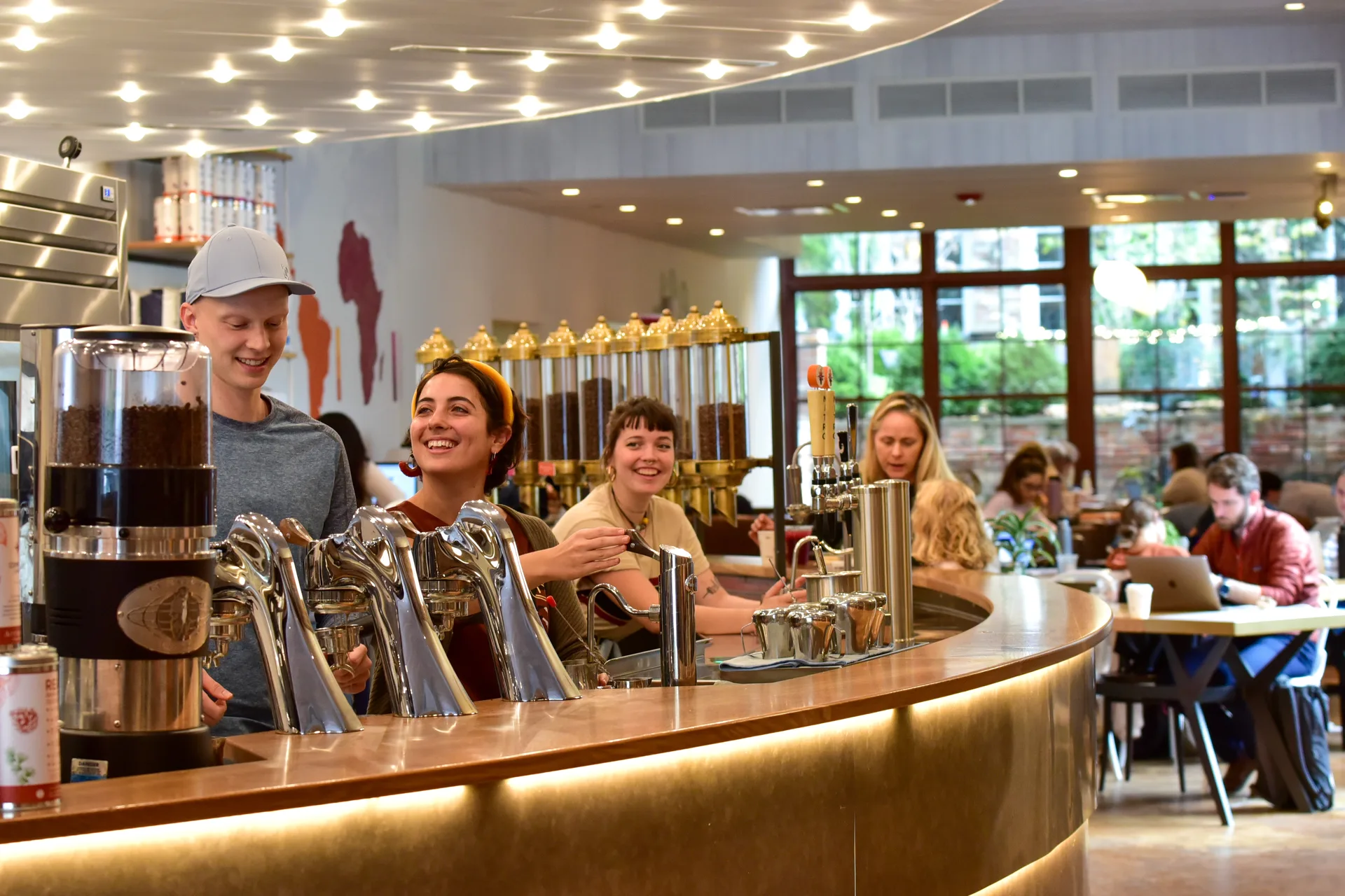 Smiling baristas behind a curved coffee bar with customers seated nearby