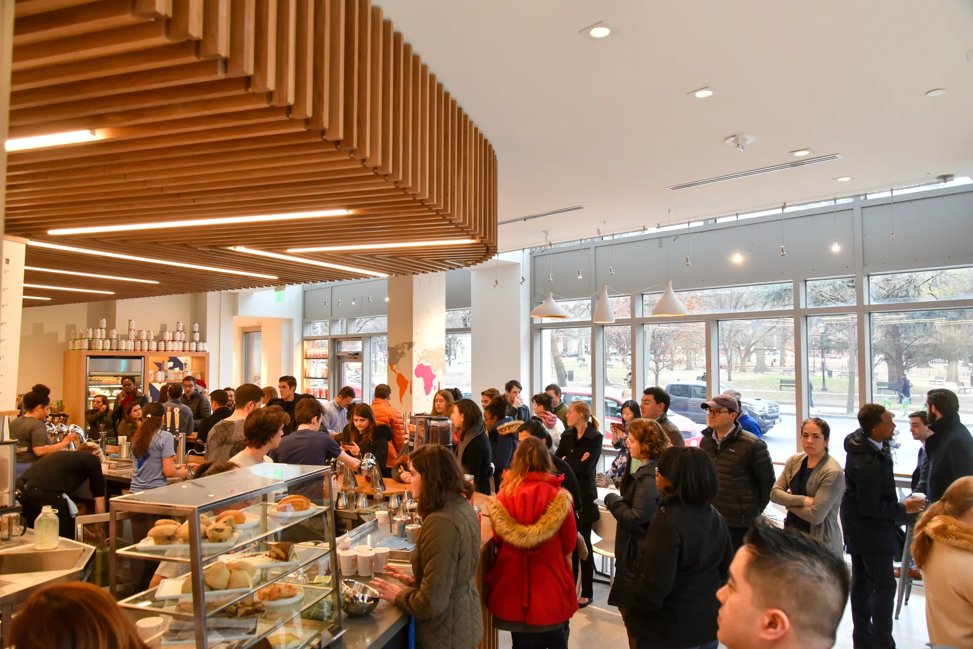 Customers gathered around a cafe counter beneath a wooden slat ceiling