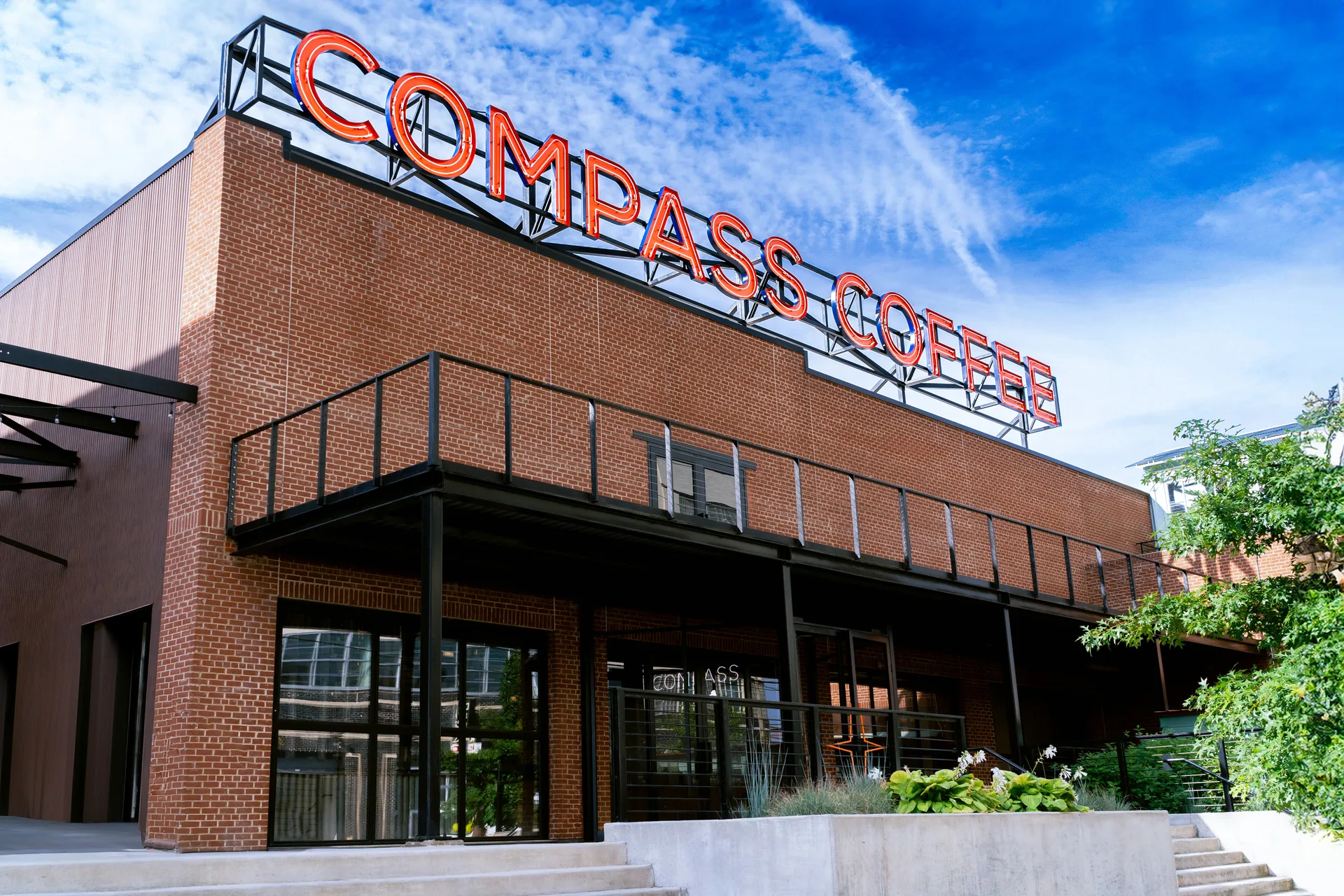Brick building with a large rooftop Compass Coffee sign against a blue sky