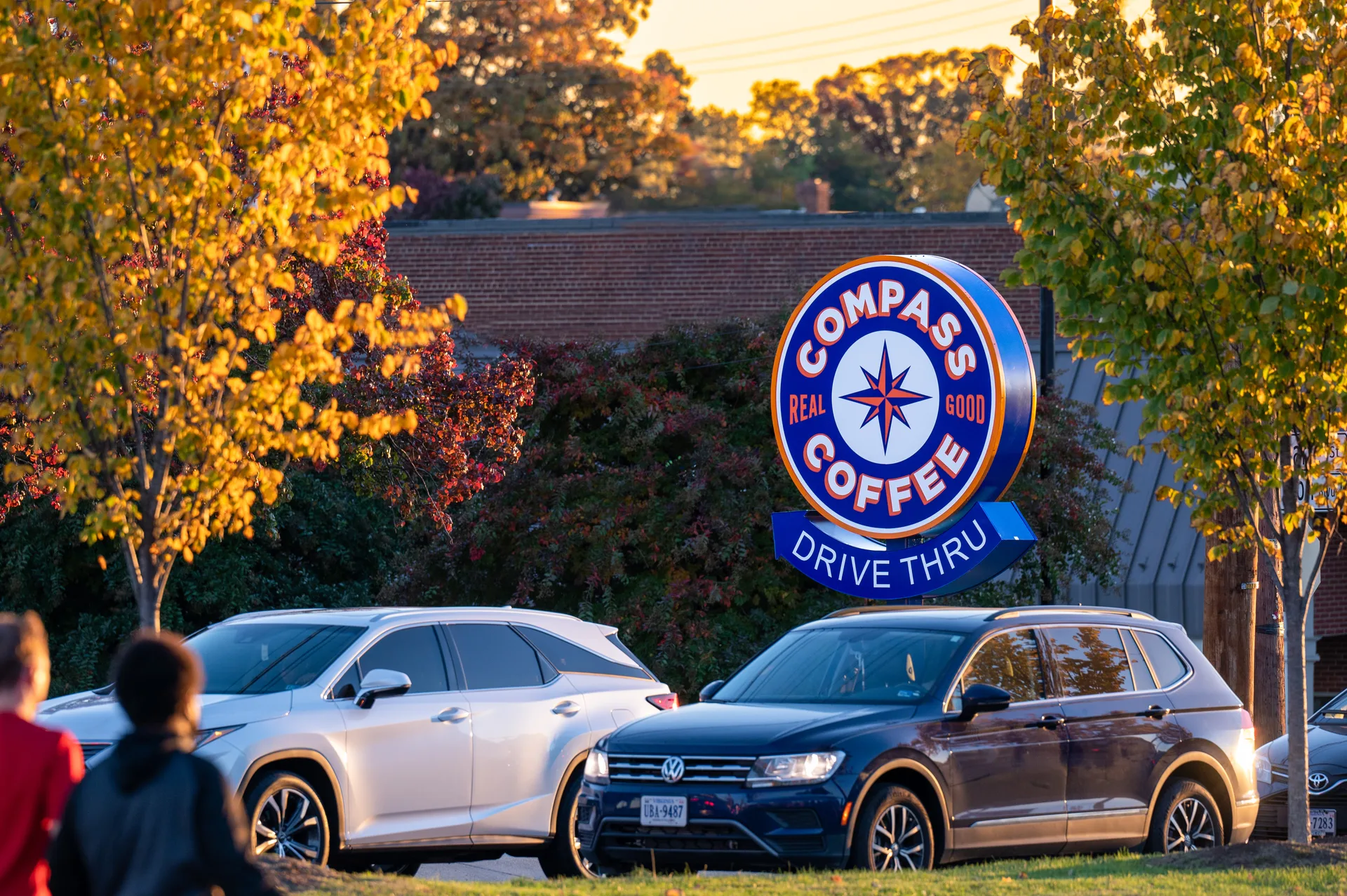 Compass Coffee drive-through sign beside parked cars and autumn trees