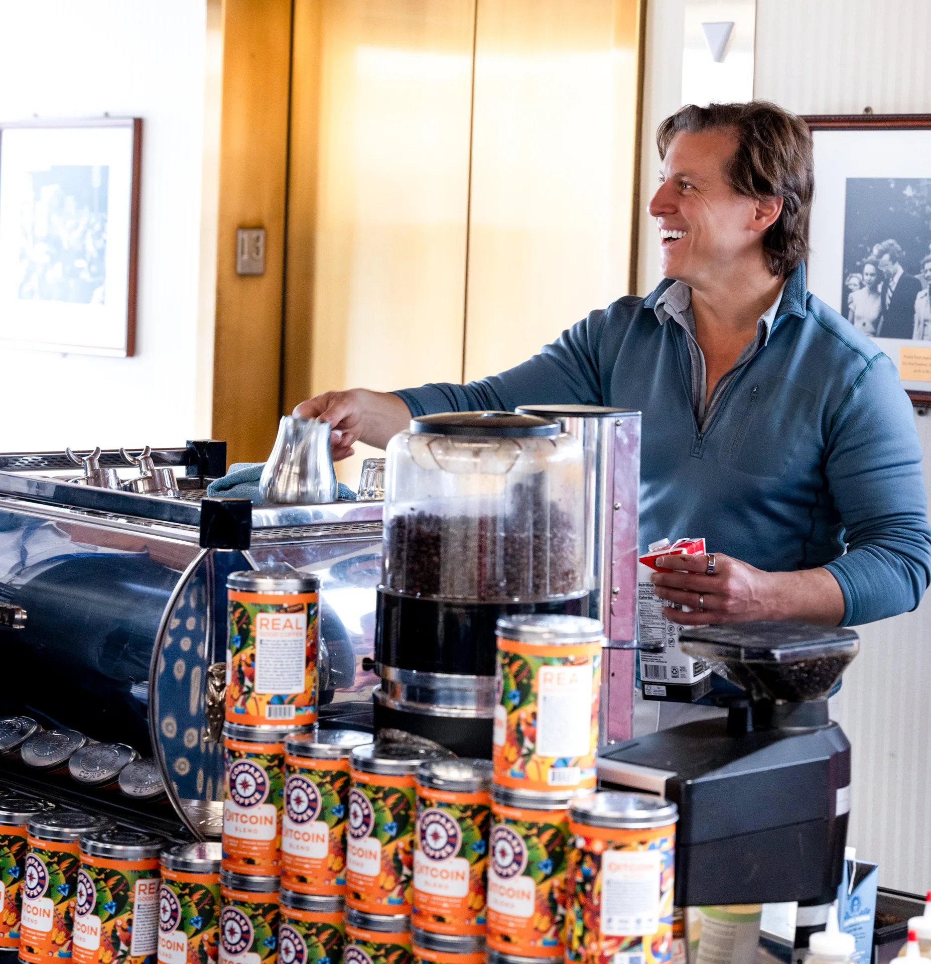 A smiling man working at an espresso machine behind stacks of coffee tins