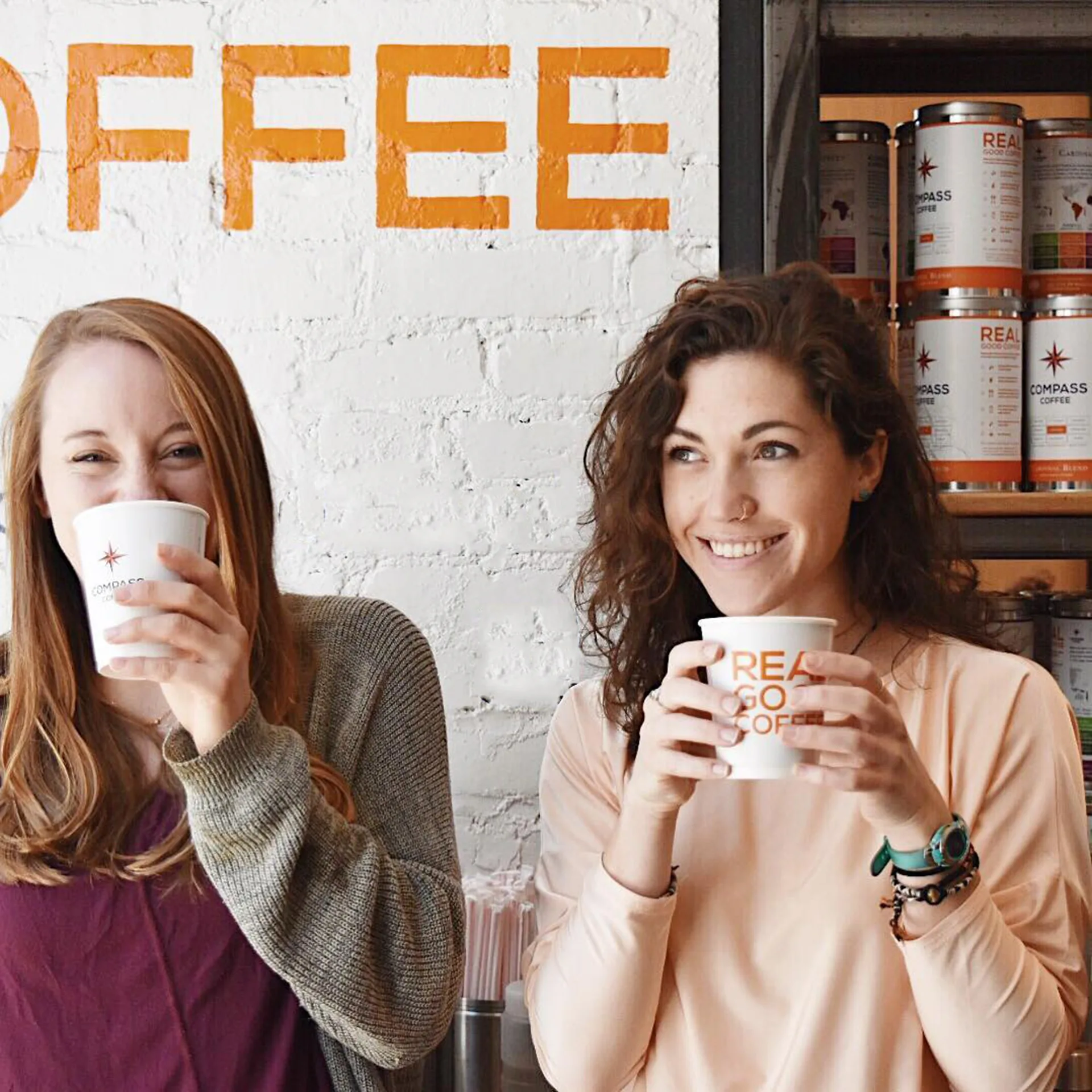 Two smiling women holding Compass Coffee cups