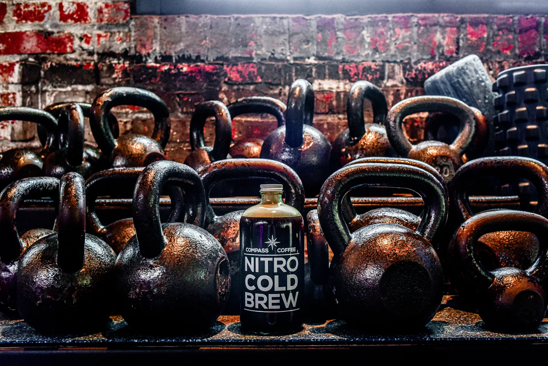 A bottle of Compass Coffee nitro cold brew among kettlebells