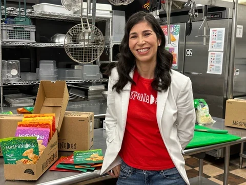 A person in a white coat beside Maspanadas packages in a commercial kitchen