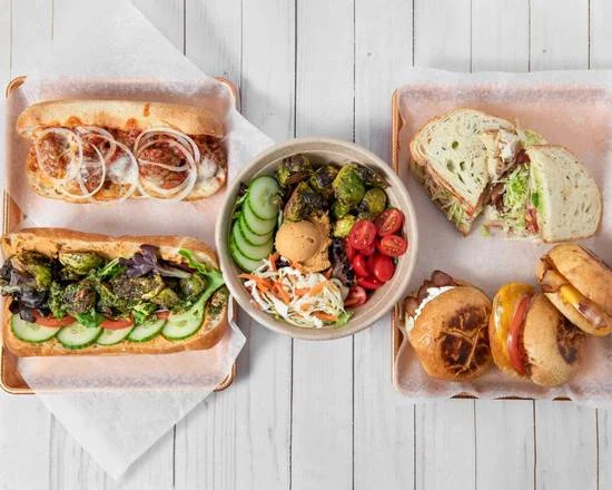 Assorted sandwiches and a bowl of salad arranged on a white table