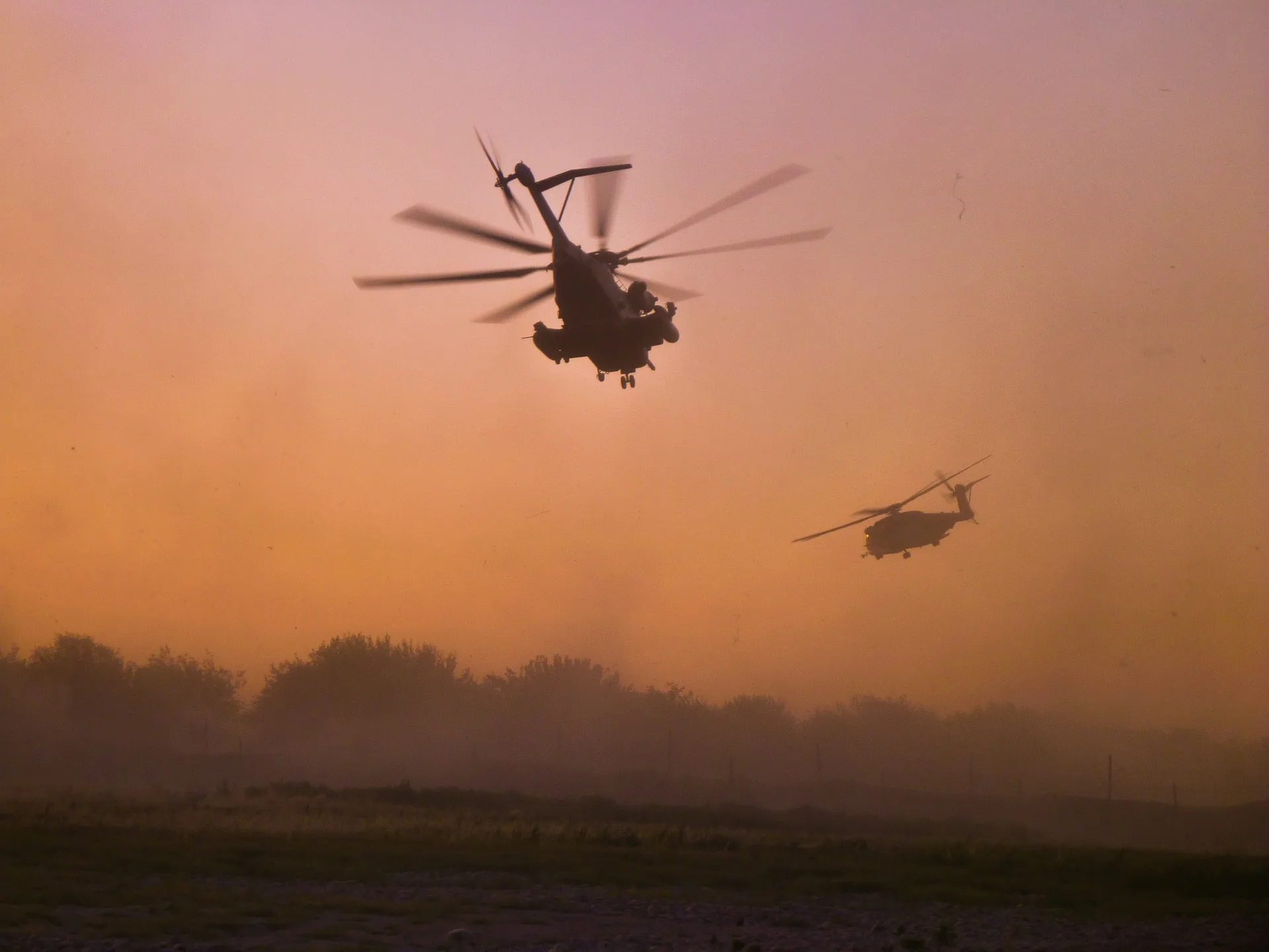 Two helicopters flying over trees in a dusty orange sky