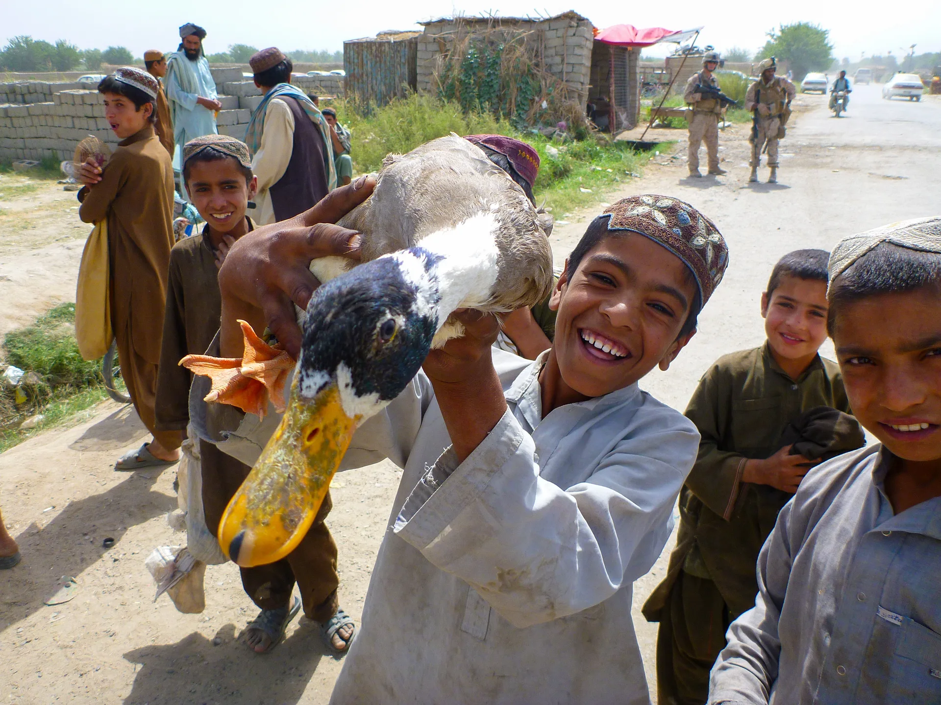 A smiling boy holding a duck, surrounded by children beside a road