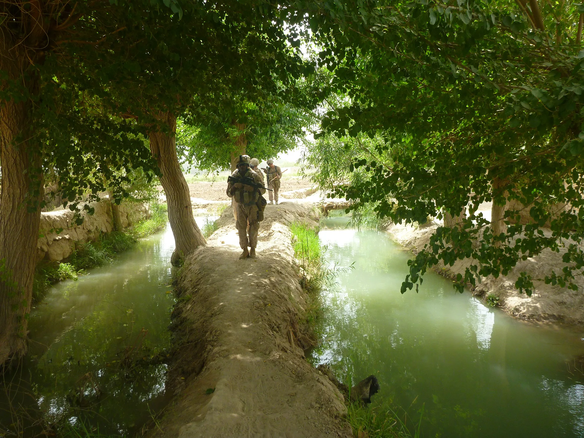 Marines walking along a shaded path between irrigation channels