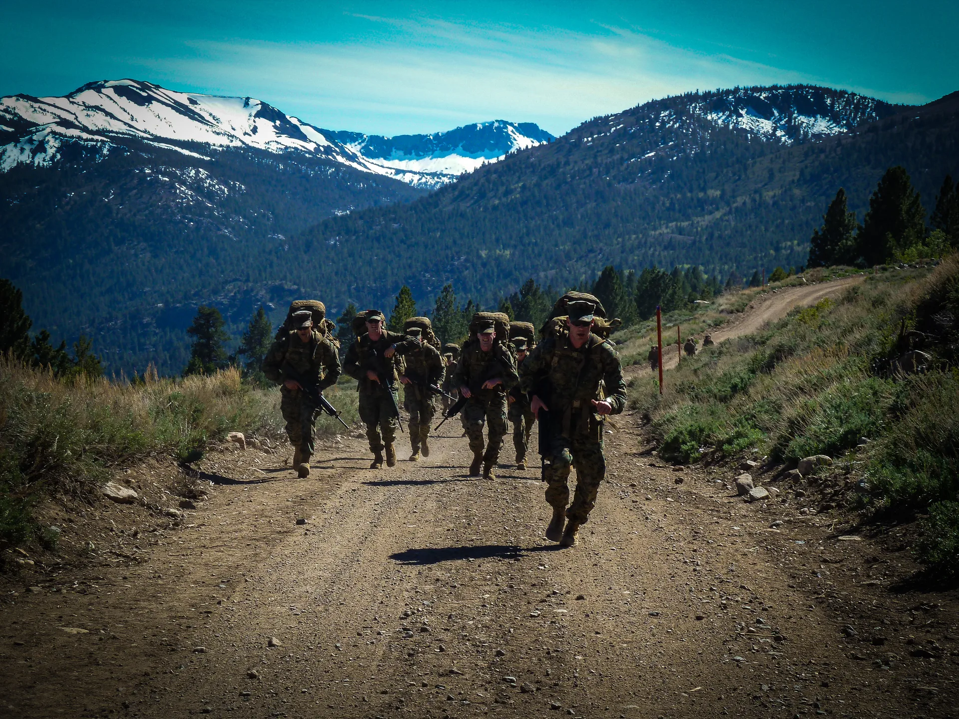 Marines carrying packs up a mountain trail beneath snowy peaks