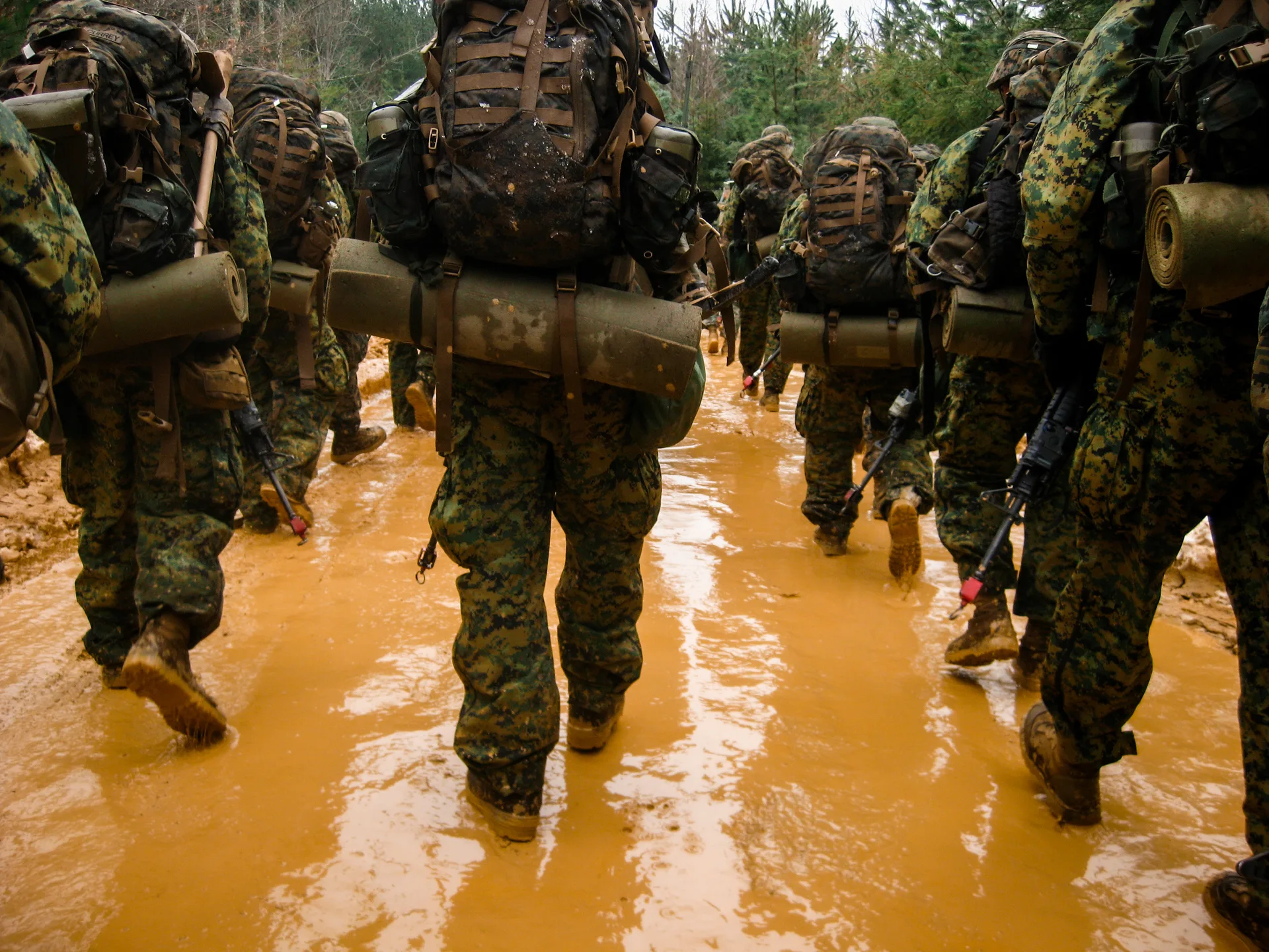 Marines with loaded packs walking through muddy water